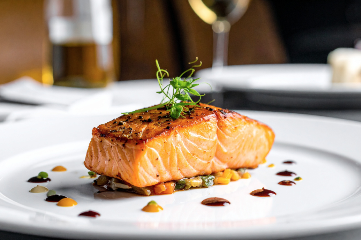 Plated salmon fillet with roasted vegetables and microgreens.