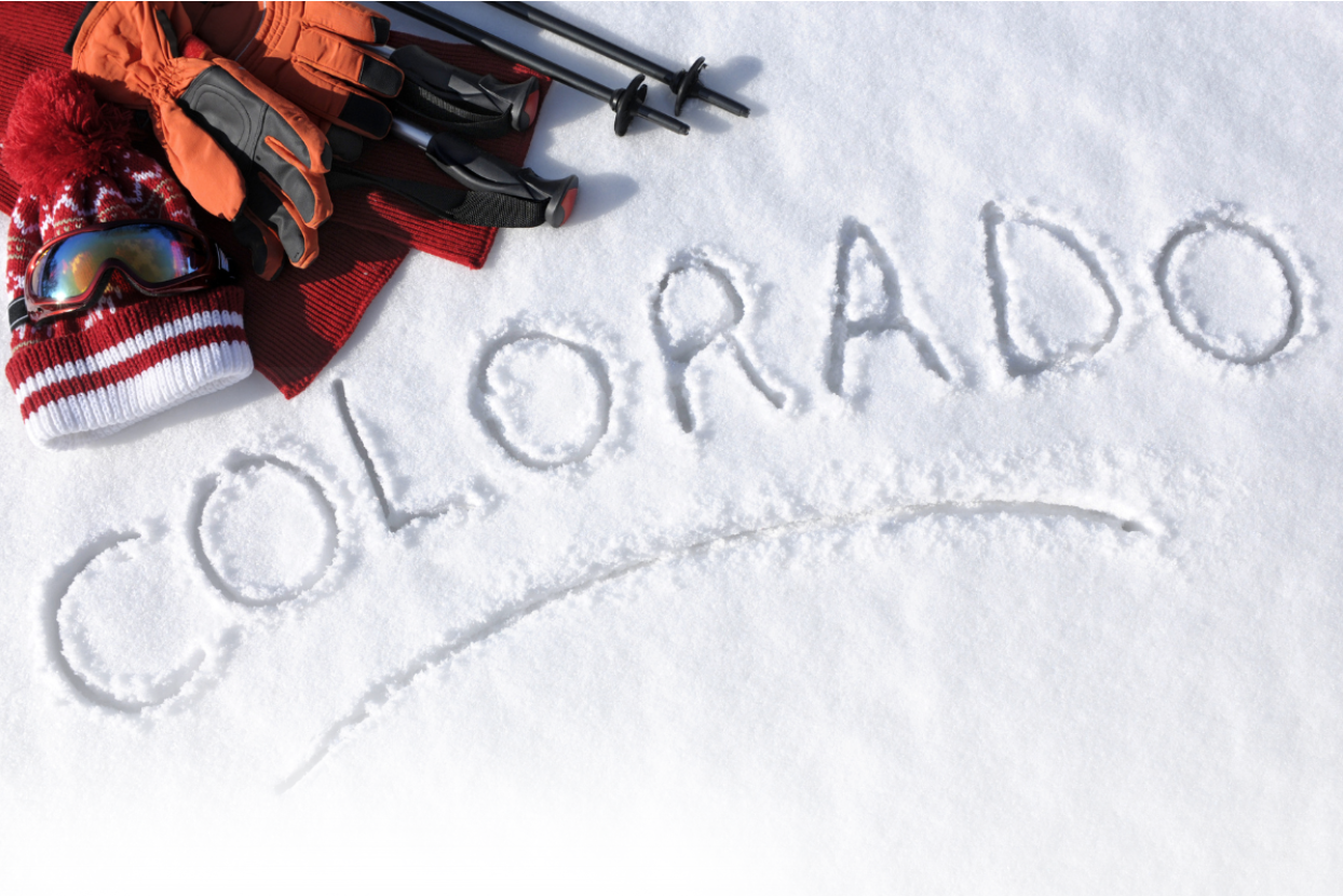 The word Colorado written in fresh snow, next to a ski equipment.